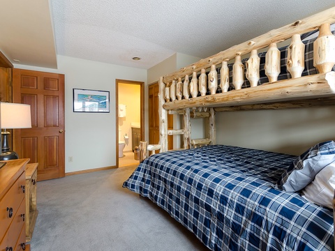 Your cozy rustic retreat features a handcrafted log bunk bed with plaid linens, warm wood furnishings, and soft lighting that creates the perfect mountain escape for restful nights.
