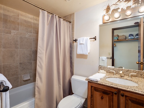 Step into your private bathroom featuring a tub-shower combo with elegant tile surround, granite vanity with ample counter space, and thoughtful touches like fresh towels and mountain-themed decor overhead.
