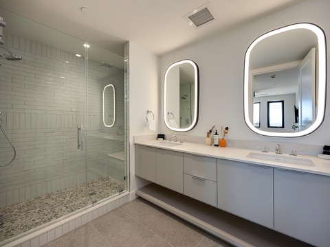Step into your spa-like bathroom, where a spacious walk-in shower and dual vanities with glowing backlit mirrors invite you to unwind in modern luxury.