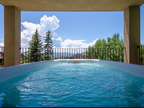 A private hot tub framed by mountain vistas, where you can soak beneath open skies, surrounded by evergreen peaks and fluffy clouds drifting overhead.