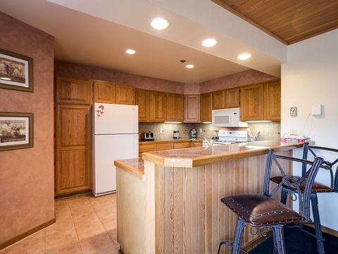 Your spacious kitchen awaits with warm wood cabinetry, modern appliances, and a breakfast bar perfect for morning coffee or casual meals together.