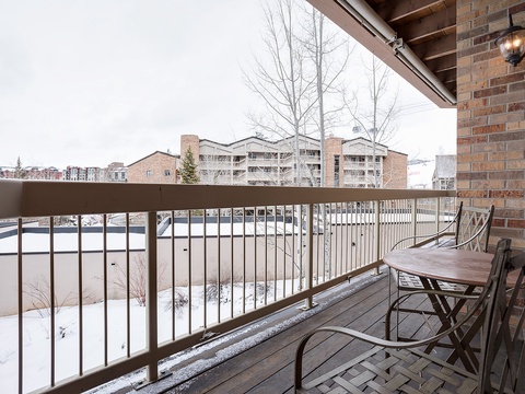 A covered balcony overlooks a snow-dusted neighborhood and nearby residential buildings, with outdoor seating ready for quiet moments enjoying the crisp mountain air.