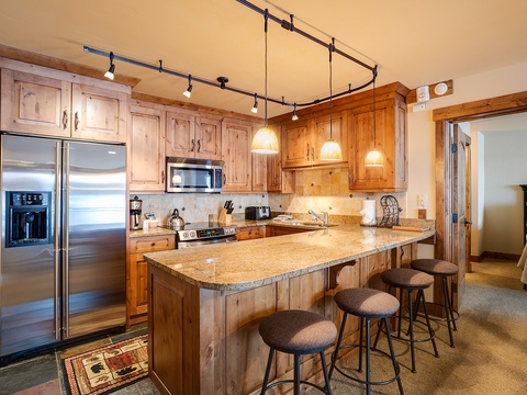 Gather around the spacious granite island with room for everyone. Warm wood cabinetry, stainless steel appliances, and pendant lighting create a welcoming space to cook, share meals, and make memories together.