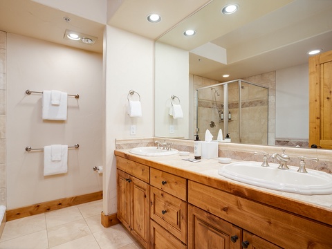 Freshen up in your spacious bathroom with dual sinks, natural wood cabinetry, and a soothing tiled shower—perfect for starting your day refreshed.