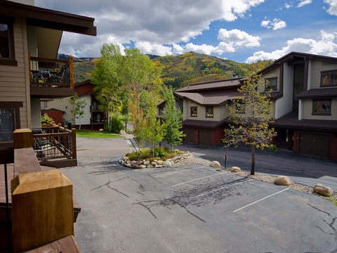 Mountain resort complex with parking and seasonal foliage set against a dramatic alpine backdrop under a partly cloudy sky.