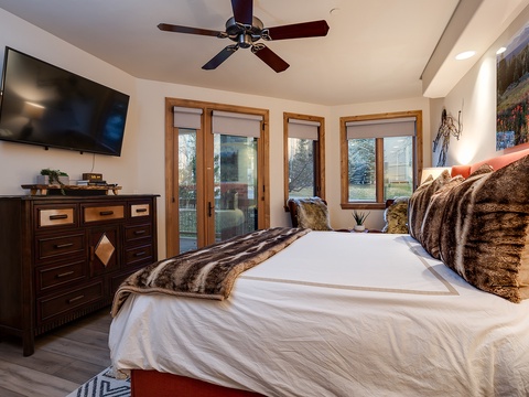Sink into crisp white linens and plush faux-fur throws in your elegant bedroom, where warm wood tones, soft lighting, and glass doors create a serene mountain retreat.