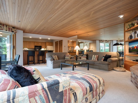Unwind in your spacious open living area with warm wood ceilings, cozy seating, and mountain views just outside. The kitchen's nearby for easy entertaining.