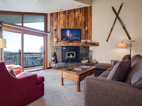 Unwind in your inviting living space featuring a cozy fireplace, plush seating, and a private balcony with mountain views—your perfect alpine retreat.