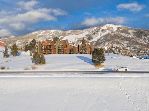 Snow-covered mountain property nestled among evergreens with scenic ski slopes in the surrounding alpine landscape.