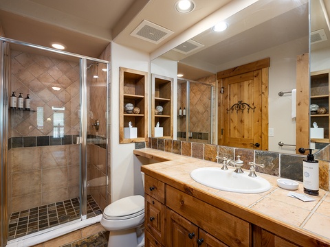 Unwind in your private bathroom with a tiled shower, rustic wood accents, and thoughtful shelving—complete with towels and amenities ready for your arrival.