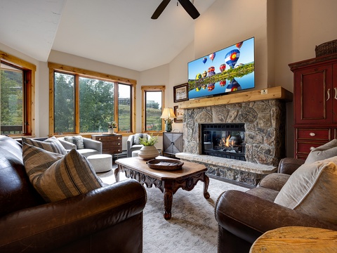 Sink into plush seating beside a crackling stone fireplace, surrounded by vaulted ceilings and sweeping natural light—your cozy retreat awaits.
