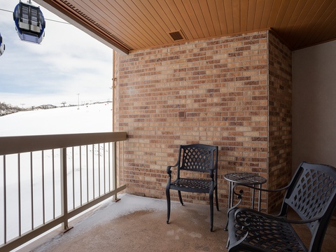 A covered balcony with seating overlooks snowy ski slopes, with gondola lifts visible above—part of the surrounding winter resort area.