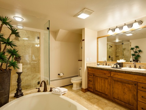 Your private spa-like bathroom features a soaking tub, walk-in shower with natural stone tile, double vanity, and warm wood cabinetry—perfect for unwinding after a day of adventure.