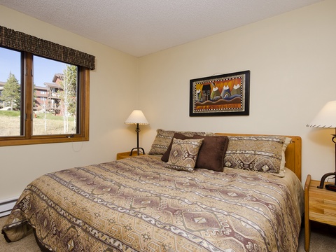 Your peaceful mountain retreat features a welcoming bedroom with warm wood accents, cozy patterned linens, and a window framing serene views of the surrounding property—perfect for restful mornings.