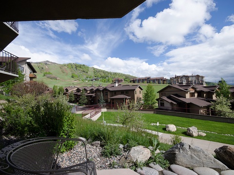 A mountain resort development nestled at the base of ski slopes, with multi-story residential buildings overlooking manicured grounds and natural landscaping in a scenic alpine valley.