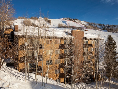 The property sits slopeside with ski runs visible in the background, framed by snow-covered aspens and surrounded by winter mountain scenery under a clear blue sky.