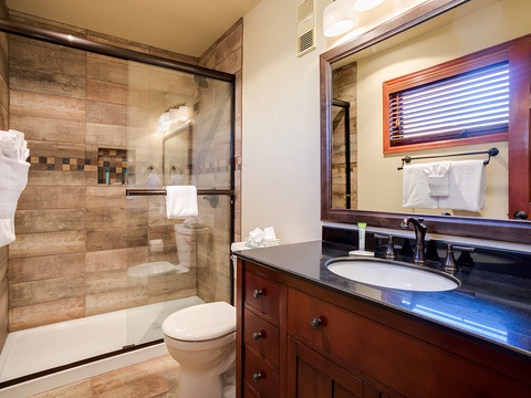Freshen up in your private bathroom with rich wood details, sleek dark countertops, and a modern walk-in shower with beautiful stone tile.