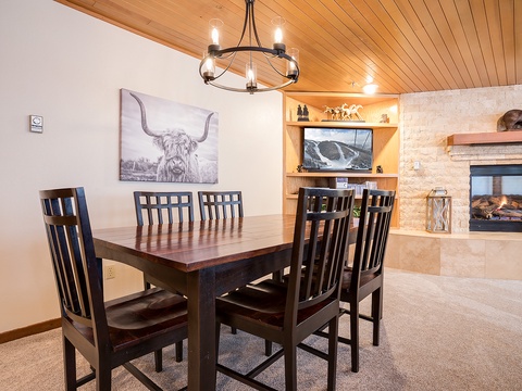 Gather around this welcoming dining table where the warm fireplace and rustic wood ceiling create the perfect backdrop for your meals and memories together.