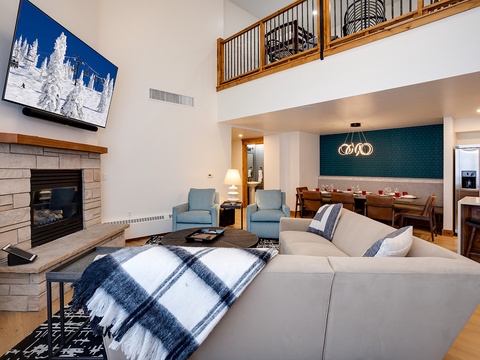 Picture yourself unwinding in this bright, open living area with soaring ceilings, a cozy fireplace, and mountain views on the big screen—your perfect alpine retreat.