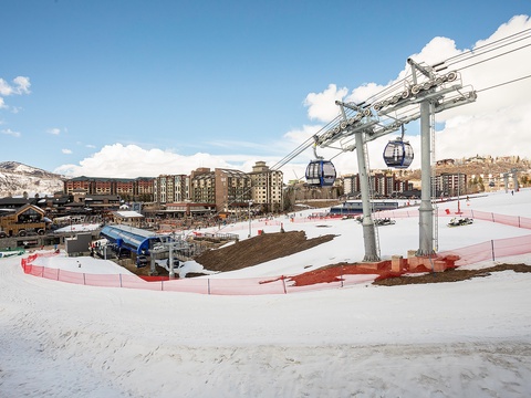 Snow-covered ski resort area featuring a gondola lift system, multi-story lodging buildings, and mountain views—a scenic winter destination with direct access to slopes and amenities.