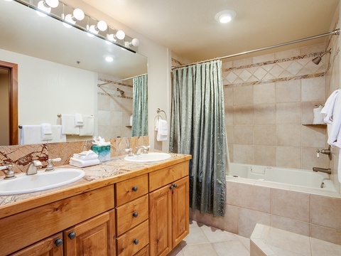 Your well-lit bathroom features dual sinks with elegant marble countertops, a tub-shower combo, and fresh towels waiting just for you—perfect for unwinding after a day of adventure.