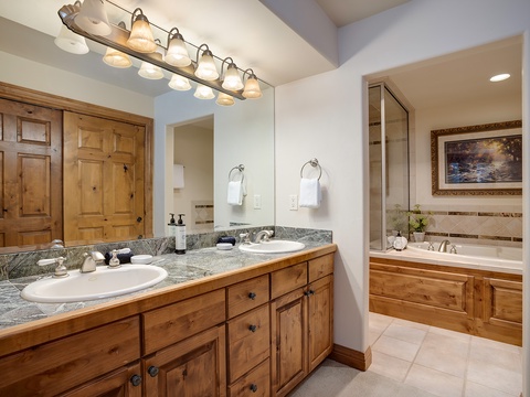 Unwind in your spacious en-suite with dual vanities, a granite countertop, warm wood cabinetry, and a soaking tub—perfect for relaxing after a day of adventure.