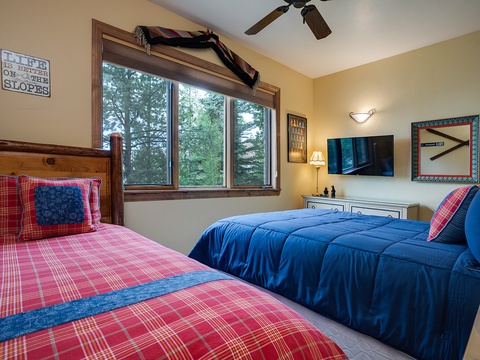 Unwind in your cozy mountain bedroom with cheerful plaid bedding, a flat-screen TV, and peaceful views of the forest canopy. A ceiling fan keeps you comfortable year-round.