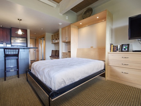 Unwind in your cozy studio retreat with a plush bed, smart storage, and a sleek kitchenette. Modern conveniences meet warm wood tones for the ultimate escape.