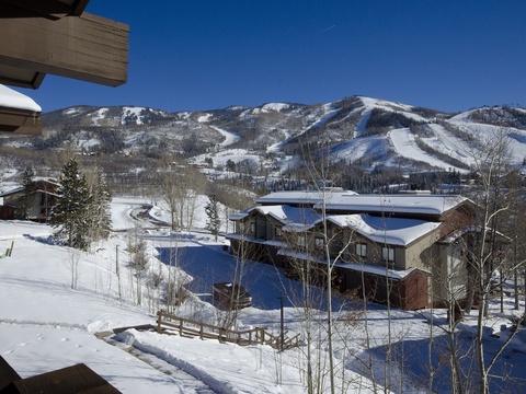 Snow-covered mountain resort with ski runs, nestled in a peaceful neighborhood surrounded by alpine scenery and evergreen trees under a brilliant blue winter sky.