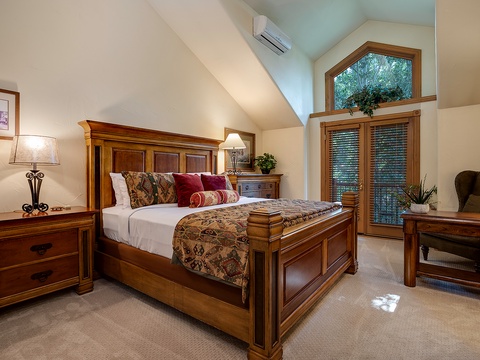 Drift off in your elegant bedroom featuring vaulted ceilings, rich wood furnishings, and private balcony access framed by leafy views—your peaceful retreat awaits.