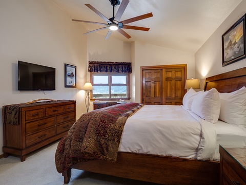 Relax in your spacious bedroom with plush bedding, warm wood tones, and a cozy ceiling fan overhead to ensure perfect comfort during your stay.