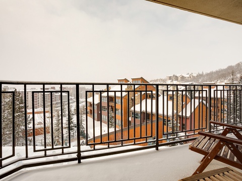 Snow-dusted balcony overlooking a peaceful winter mountain village, with rustic lodges nestled among evergreen trees and a quiet alpine landscape stretching into the distance.