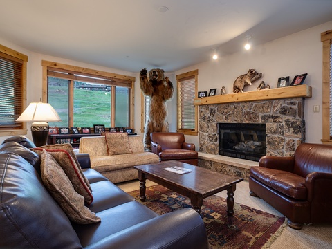 Gather around the stone fireplace in this inviting living room, where rustic charm meets comfort. Large windows frame mountain views while leather seating and warm wood tones create your perfect retreat.