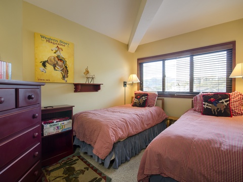 Unwind in your cozy twin bedroom, where vintage Western charm meets comfortable bedding. Natural light floods the space through large windows, creating a warm retreat for restful nights.