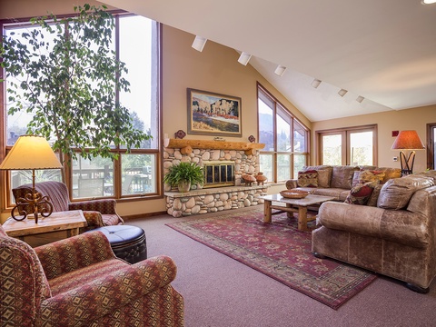 Sink into plush sofas by the stone fireplace and let natural light from floor-to-ceiling windows warm your mountain retreat—your perfect spot to unwind after a day exploring.
