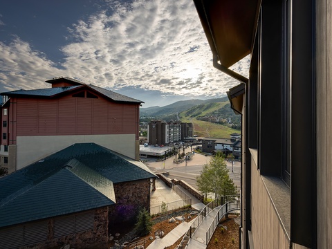 A daytime view overlooking nearby buildings and the surrounding mountain landscape, framed by the property's balcony edge.
