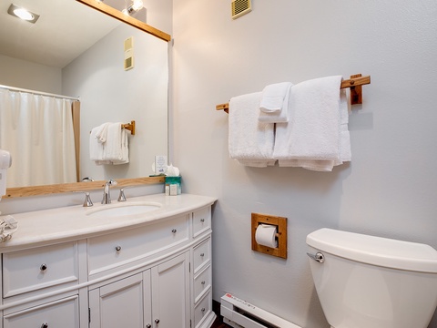 Your private bathroom features fresh white linens, a spacious vanity with plenty of storage, and warm wood accents that create a welcoming, home-away-from-home feel.