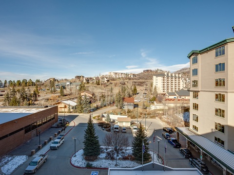 A sunny mountain town setting with surrounding hillside residences and convenient parking facilities, offering easy access to nearby attractions and scenic landscapes.