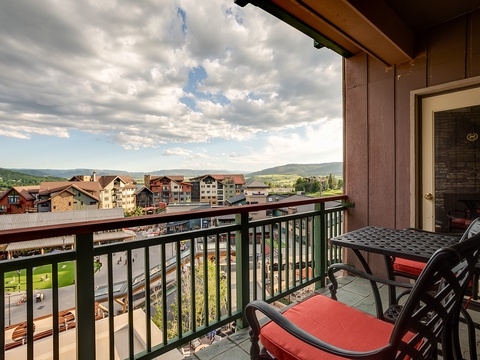A covered balcony overlooks a resort village nestled against rolling green hills, with comfortable seating offering front-row seats to dramatic mountain sunsets and valley vistas.