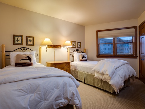 Sink into plush white comforters after your mountain adventures. Two cozy beds frame a warm glow, while peaks peek through the window to inspire tomorrow's plans.