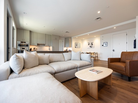 Sink into plush seating in your stylish open-plan living area, where modern design meets warm wood tones. The sleek kitchen invites you to cook together, while sunlight pours through floor-to-ceiling windows.