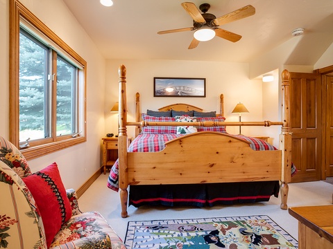 Relax in your cozy bedroom with pine furnishings, plaid bedding, and a ceiling fan. Enjoy peaceful lake views through large windows and unwind in rustic mountain charm.