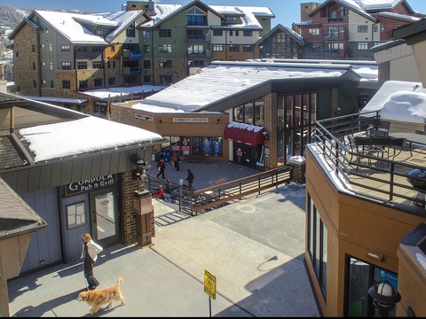 Elevated view of the surrounding village area during winter, featuring nearby shops, restaurants, and snow-covered alpine buildings that frame the resort neighborhood.