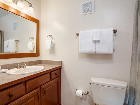 Your private bathroom features warm wood cabinetry, fresh white towels, and thoughtful details that make your stay comfortable and convenient.