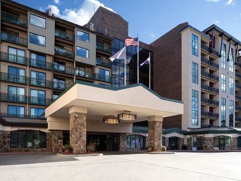 Multi-story property with stone-columned entrance, balconies on each level, and flags welcoming guests to the main building.