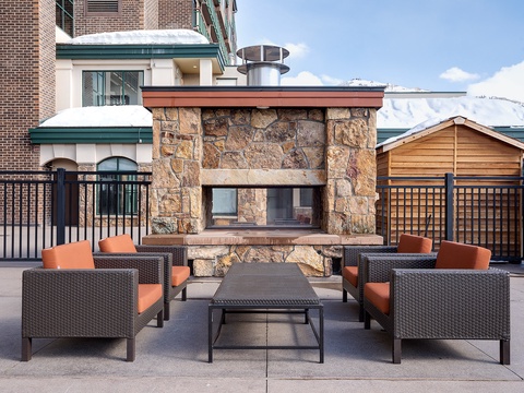 Mountain vistas frame this rooftop terrace featuring a stone fireplace, plush wicker seating, and modern comforts—your alpine escape awaits.