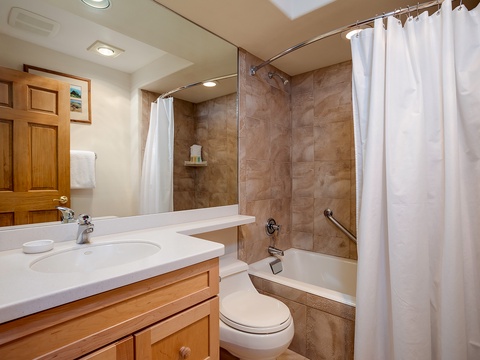 Step into your private bathroom featuring warm wood cabinetry, neutral tones, and a relaxing tub-shower combo—your personal retreat after mountain adventures.