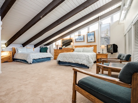 Unwind in your spacious loft bedroom with vaulted ceilings, exposed beams, and two cozy beds. Soft linens, warm wood furniture, and a relaxing seating area await your retreat.