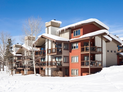 A snow-covered mountain retreat with warm wood tones and expansive balconies, offering winter getaway charm surrounded by pristine evergreens and ski country beauty.