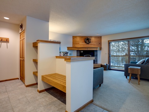 Cozy open-concept space with warm wood accents, a stone fireplace, and serene forest views—your perfect mountain retreat awaits.